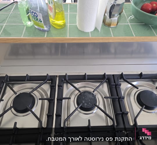 כיריים עם בקבוקי חומרי ניקוי ועגבניות בקערה ירוקה